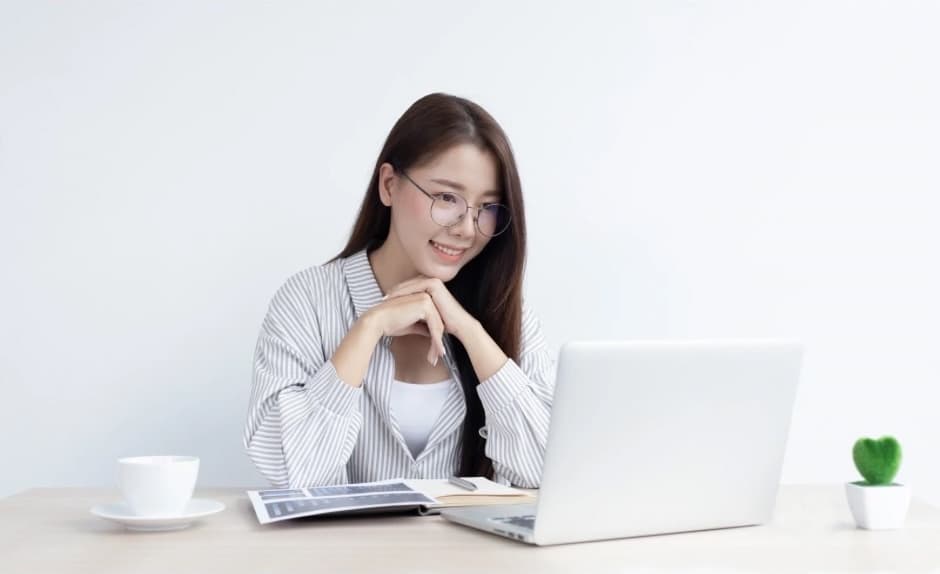 A woman sitting at a desk, smiling at her laptop.